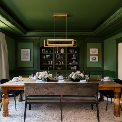 A dining room with two-tone green walls and modern gold light fixture