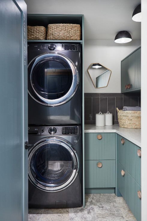 Stacked washer and dryer in laundry room with blue cabinetry