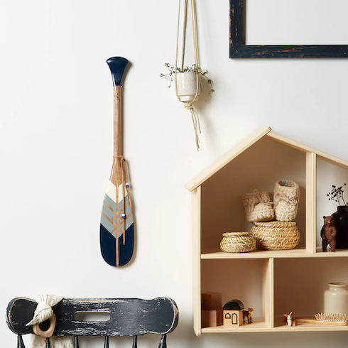 La Guerrière ornamental paddle from Onquata Native Paddle hangs on a white wall beside a wooden house self and a ceramic macramé plant holder as featured in HGTV’s Canadian Gift Ideas from Homegrown Small Businesses for Under $100