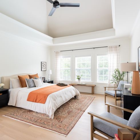 Light, white master bedroom with soft orange accents