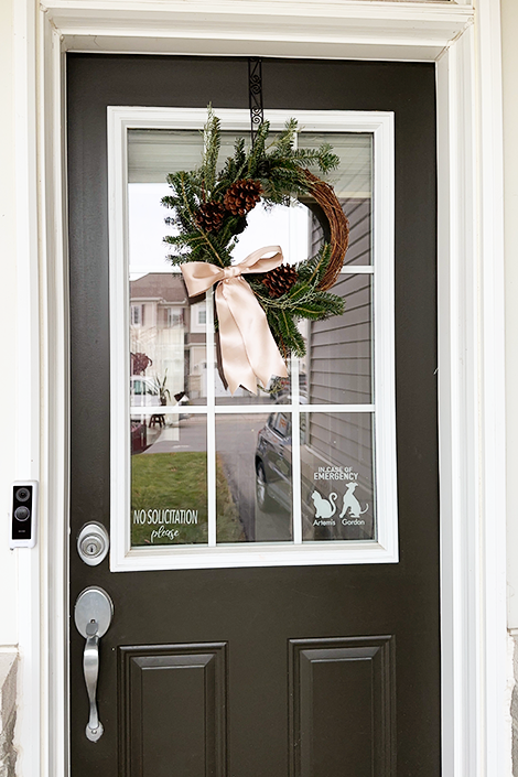 a green wreath on a grapevine base with a champagne bow hangs on a black door - wreath tutorial