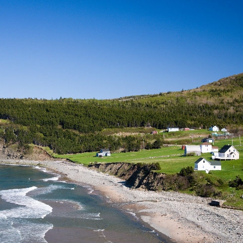 A beachside area in Cape Breton, Nova Scotia with a few houses and cliffs in the background