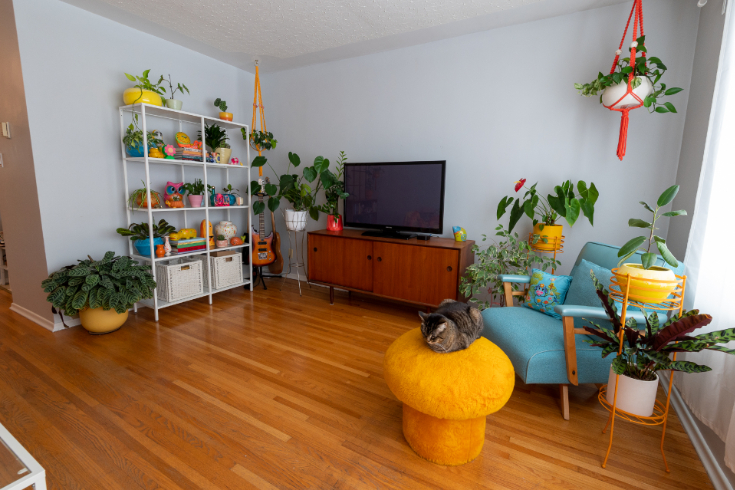 A wide shot of the midcentury modern-inspired living room with MCM TV hutch, blue chair and yellow mushroom stool