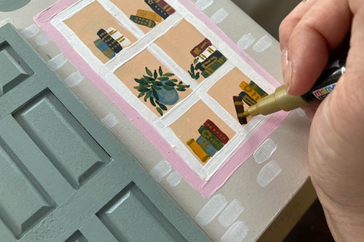 A person drawing books on their storefront DIY dollhouse nightstand 