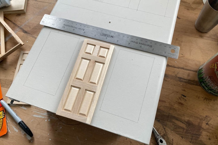 A person adding a door to their DIY dollhouse nightstand 