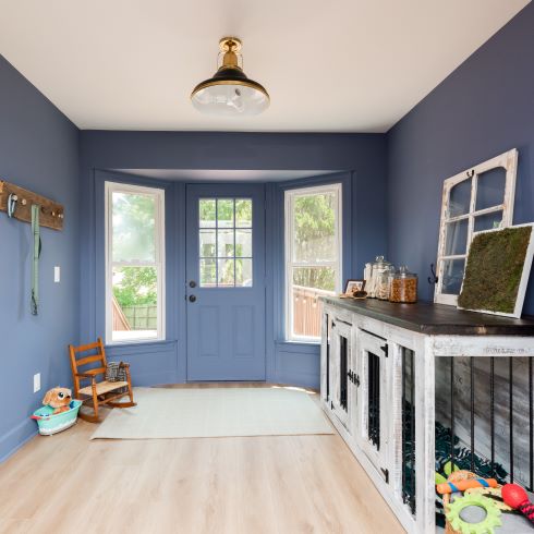 Rear entryway with soft blue walls, light hardwood flooring, and large custom dog crate