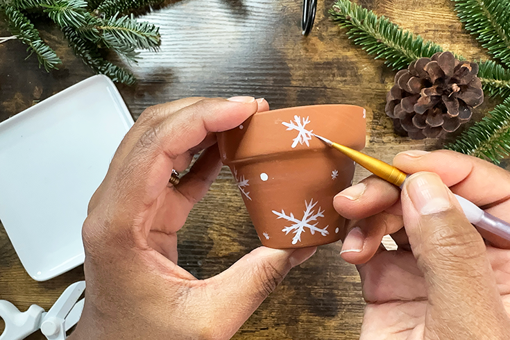 A person's hands as they paint white snowflakes on a terracotta pot