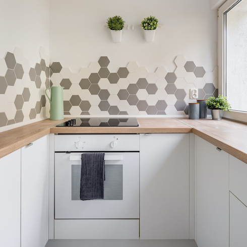 Kitchen in nordic style with white cabinets, wooden countertop and hexagonal wall tiles