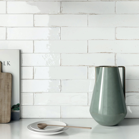 Tiles Inspired Matisse Bianco Zellige-style ceramic and a more traditional subway format with an intentional weathering glazed on the edge of the tiles as featured in a white kitchen withe a green jug and a plate on a white countertop