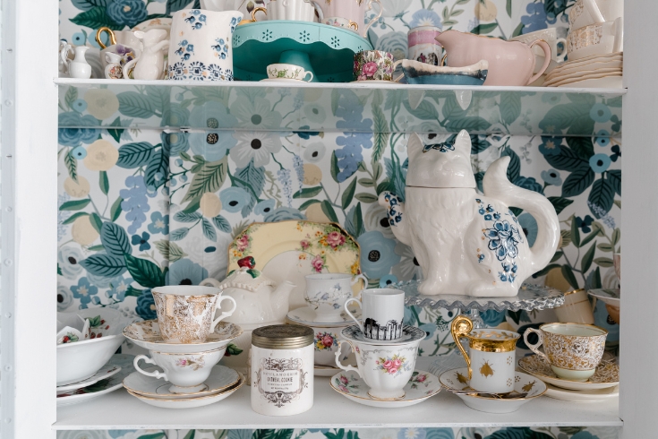 Teacups on the shelf of a vintage hutch.