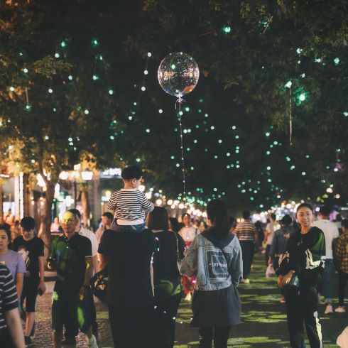 Festival-goers on a street illuminated by small overhead lights