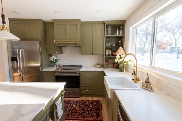 A kitchen with a large window, green cabinetry, gold fixtures and quartz countertops