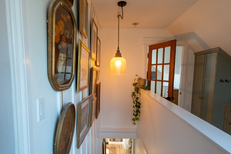The top landing of a stairway with a wall displaying vintage art on the left hand side