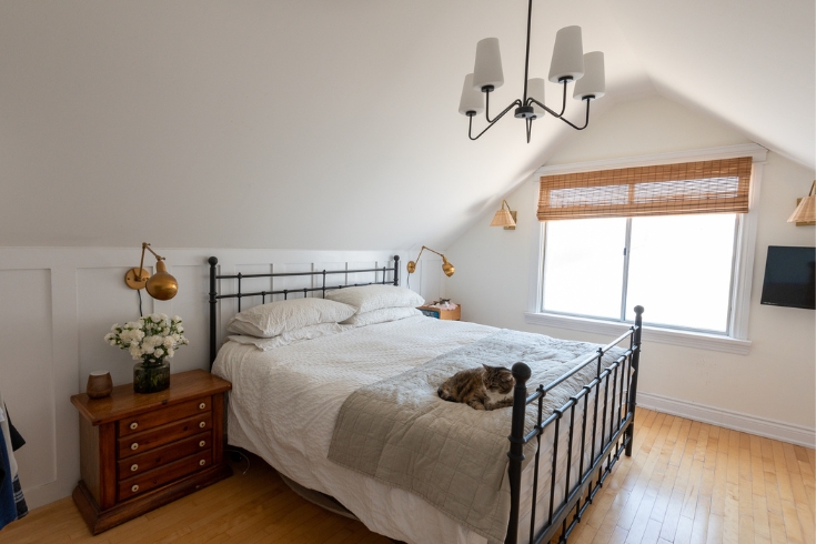 A large primary bedroom with sloped ceilings, large window, and a cat on the bed