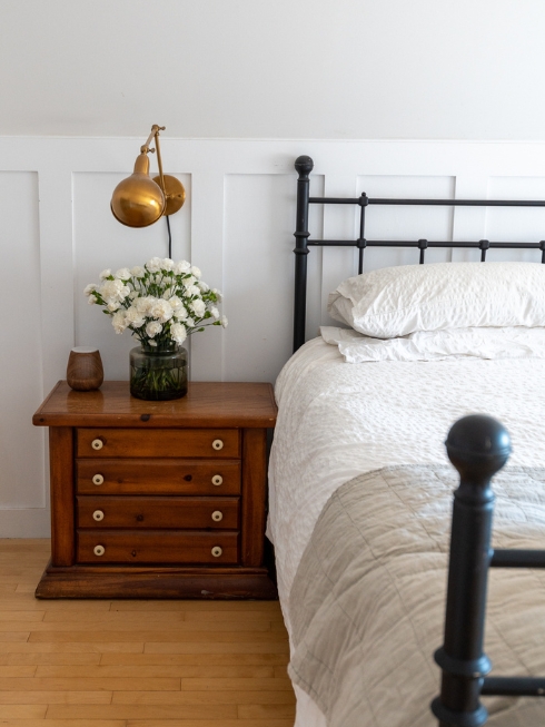 A black iron headboard, bed and side table against a white wall with panelling