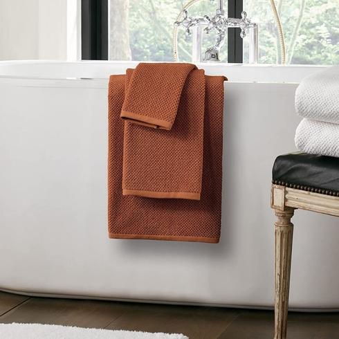 Three orange bathroom towels on a bathtub White cotton throw on bed - Nate Home by Nate Berkus collection
