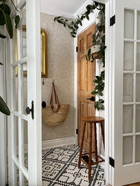 An entranceway with door, crawling plant, mosaic tile flooring and a straw bag hanging on the wall