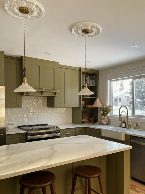 A kitchen with green cabinets, quartz countertops and two pendant lights