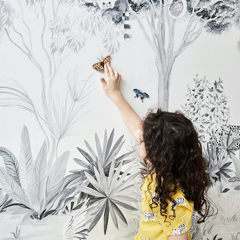 A girl pushes two magnetic butterflies up a wall covered in a Magnetic Jungle Wallpaper Mural by SianZeng found on Etsy Canada