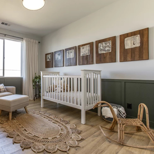Gender neutral nursery by designer Jasmine Roth for HGTV Canada with green wood panels, a white crib, a unique wicker rocking horse and recycled wood frames on the wall.