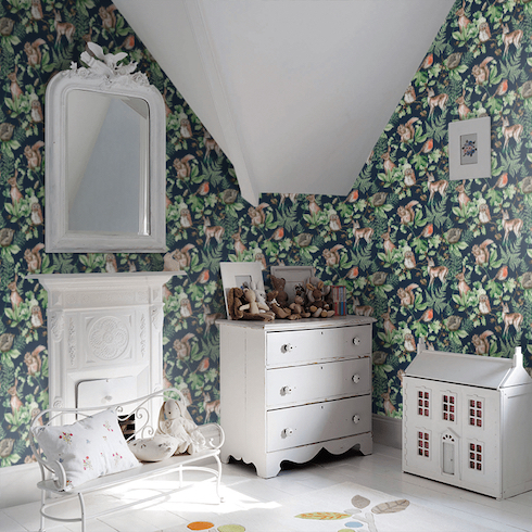Child’s room with a wallpaper from Superfresco Easy Individual Kids@Home Wallpaper Collection called Woodland Animals found at WallpaperDirect, as well as a small white antique dresser, dollhouse and child-sized bench.