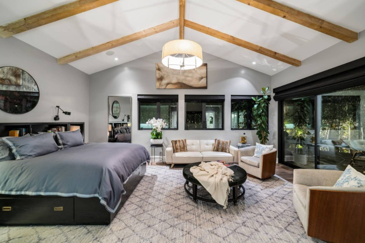 A bedroom with vaulted ceiling, a bed, seating area and large windows
