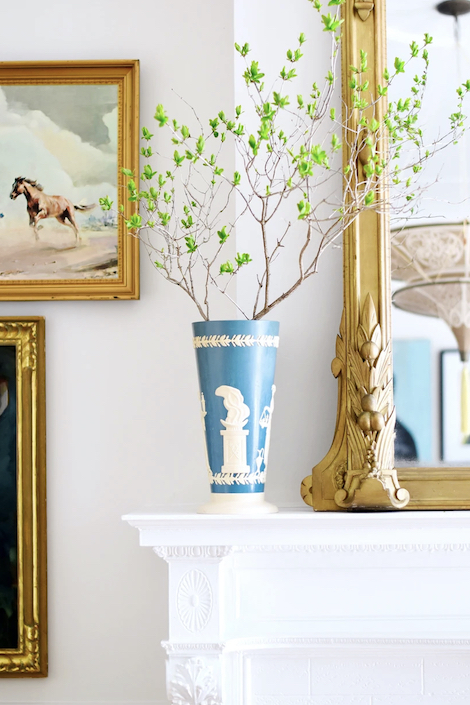 Antique blue and white vase with a green branch sits on a mantle in front of antique gold framed mirror and art designed by Cynthia Zamaria