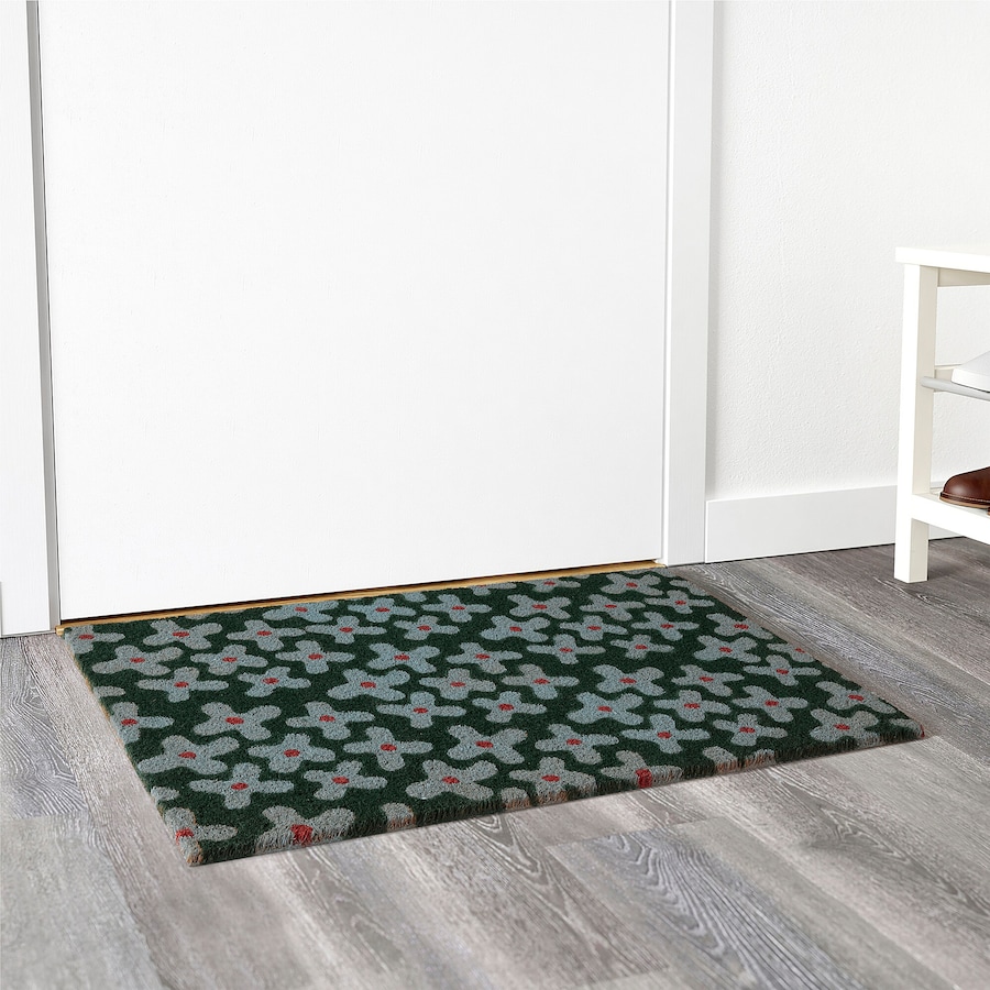 A dark green floral front door mat on a grey hardwood floor