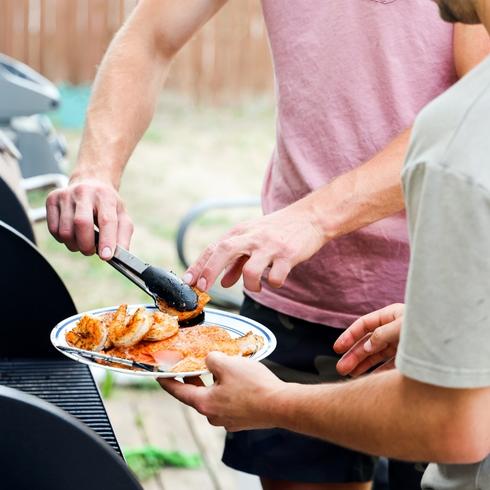 Friends grilling food outdoors at a backyard party.