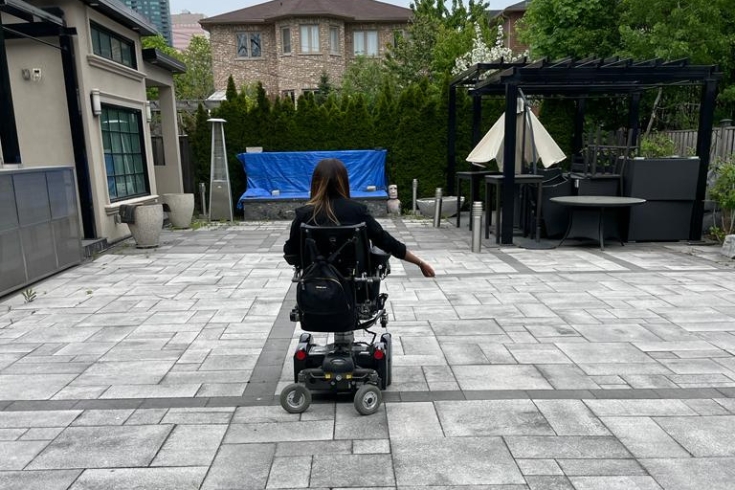 Woman in wheelchair in her paved backyard 