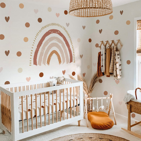 A light coloured nursery with large rainbow decal, plus hearts and polka dots with a white basinet and wooden fixtures