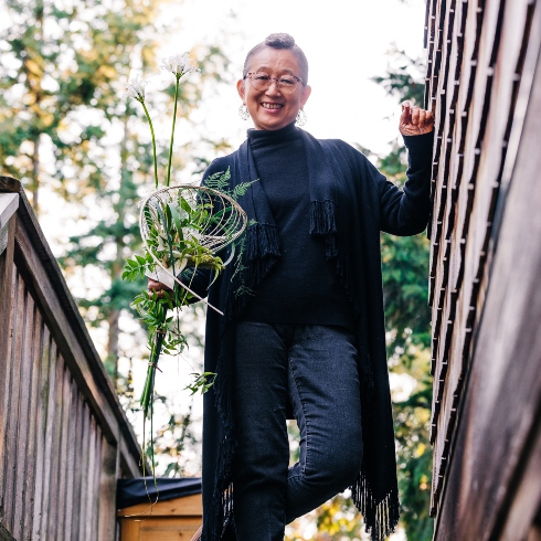 Floral artist and educator Hitomi Gilliam holding a plant while standing on an outdoor staircase
