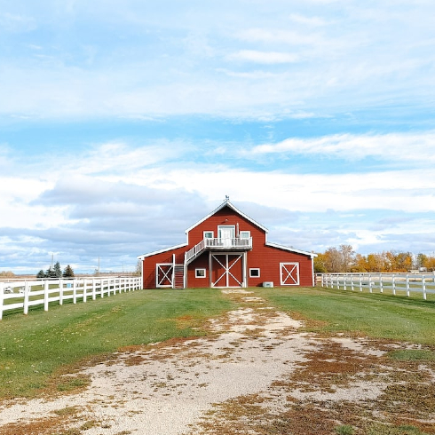 A stunning exterior shot of a red barn down a country road on a bright sunny day