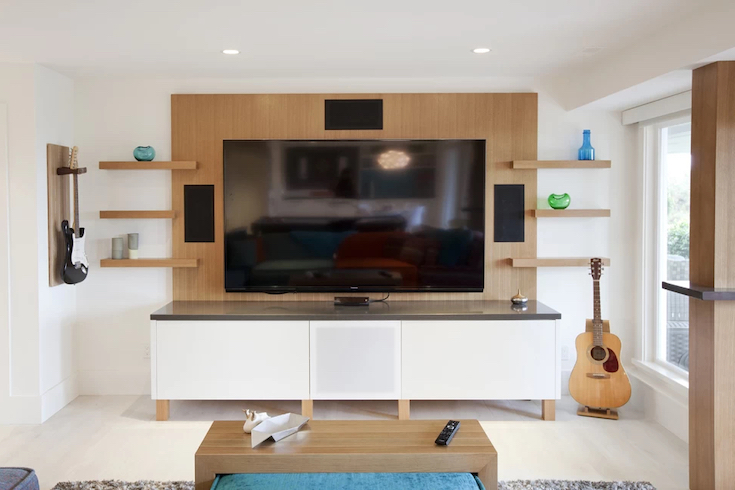 Modern family room with a large TV on a wood lined wall in a different wood tone to the wood flooring, with a coffee table and a guitar in the corner.
