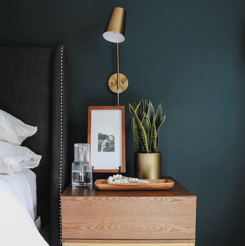 Sherwin-Williams Cascades SW 7623, a dark, majestic blue paint colour, exudes a rich and mysterious personality with its swirl of grey, yellow and blue undertones featured on the walls of the chic small bedroom with a side table and upholstered headboard