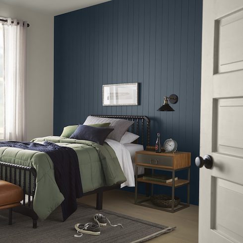 Cool small bedroom featuring Behr paint colour Midnight, a black framed bed with green and blue bedding, and a grey floor with an area rug with a pair of shoes on it.