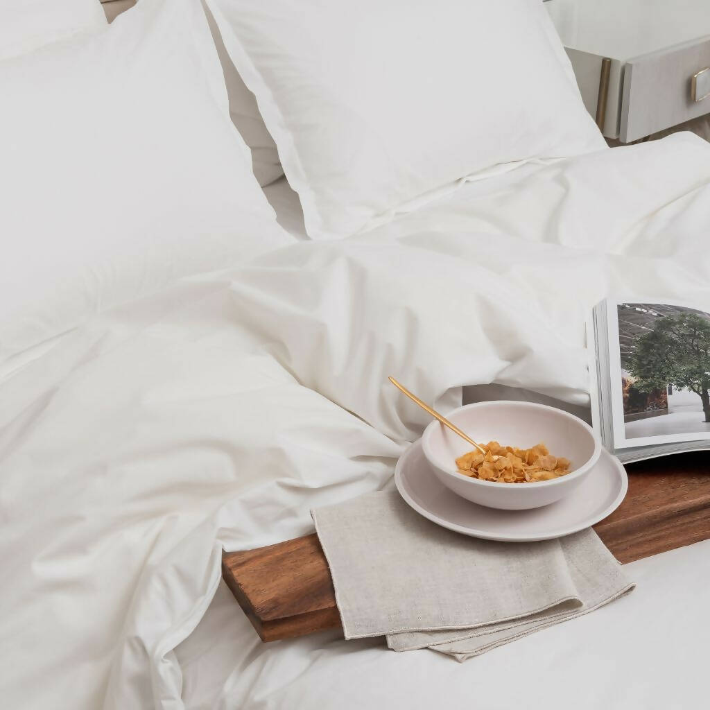 White sheets and white pillows on a bed with a food tray and book.