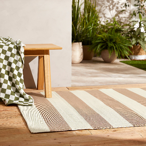 A tan and cream striped outdoor rug on a wooden patio