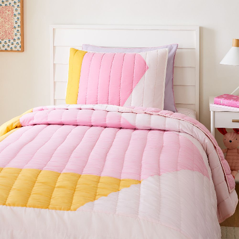 A bed with a bright pink, yellow and white bedspread