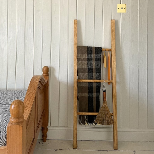A wooden blanket ladder leaning against a bedroom wall at the foot of a bed