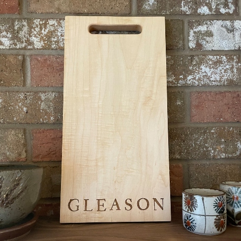 An engraved wooden cheese board leaning against a brick wall.