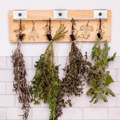 A kitchen herb drying rack with four hooks holding different hanging herbs