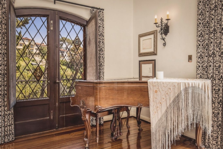 An antique piano in front of French doors that look out to the Los Feliz hills in Los Angeles