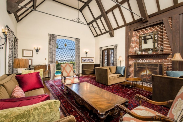 A two-storey living room with vaulted ceilings, wooden beams and panelling, a brick fireplace and antique furnishings.