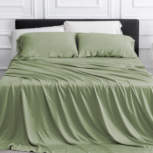 Green sheets on a bed with white panelled wall behind it.