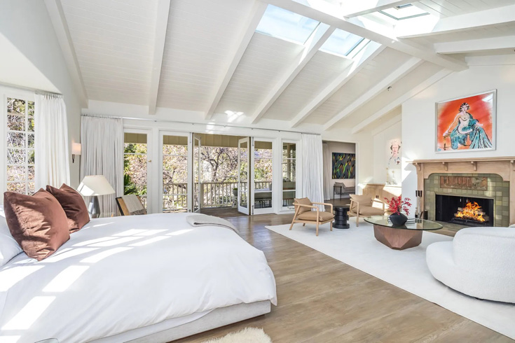 A bright and open bedroom with a slanted roof, fireplace and cozy bed.
