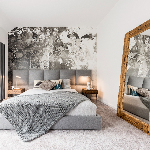 King-size bed with gray square headboard, large rustic wooden mirror and textured wall in trendy minimalist apartment
