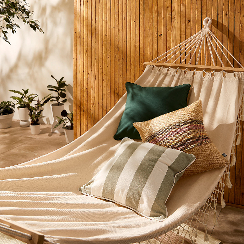 A natural hammock with three accent pillows hangs in a dreamy outdoor space