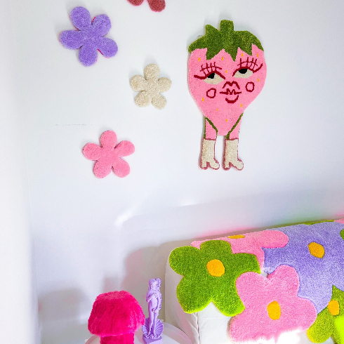 A shot of a bedroom with funky tufted wall art: small flowers and a strawberry with boots