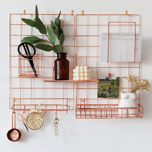 A rose gold wall grid with various office supplies, art work and plants